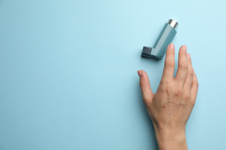 Woman holding asthma inhaler on light blue background, top view. Space for textの写真素材