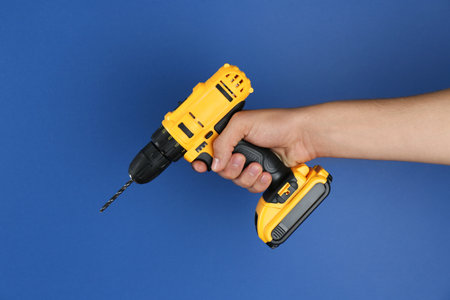 Man with cordless electric drill on blue background, closeupの写真素材