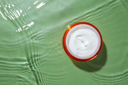 Cosmetic product. Jar with cream in water on light green background, top view. Space for textの写真素材