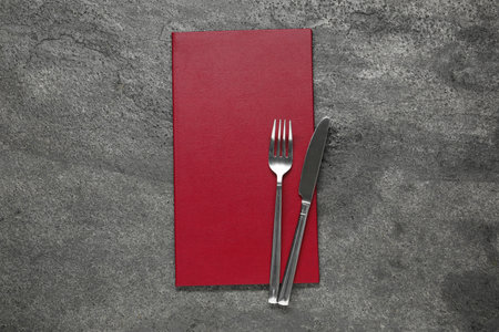 Hardcover menu and cutlery on gray textured table, top viewの写真素材