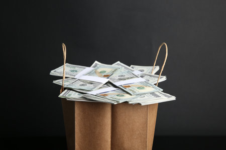 Dollar banknotes in paper bag on black background, closeup