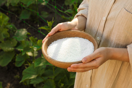 Woman holding plant fertilizer in bowl outdoors, closeup