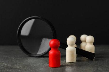 Red piece among wooden ones and magnifying glass on gray tableの写真素材