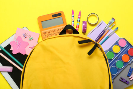 School backpack and stationery on yellow background, flat lay