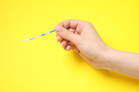 Woman holding pregnancy test on yellow background, closeupの写真素材