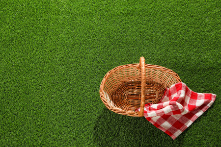 One picnic wicker basket with checkered napkin on green grass, top view. Space for textの写真素材