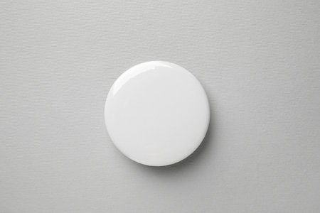 Blank white button badge on gray background, top view. Mockup for design