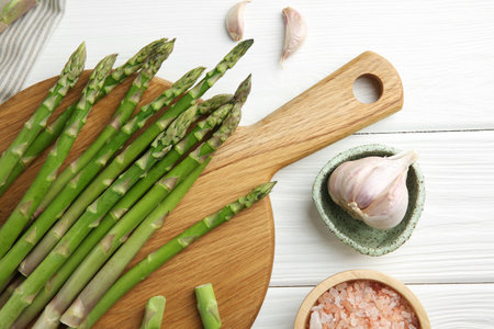Fresh green asparagus stems, garlic and sea salt on white wooden table, flat layの写真素材