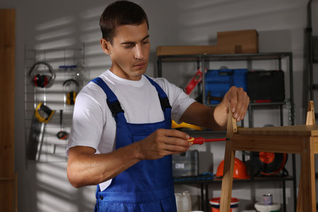 Man repairing wooden stool with screwdriver indoorsの写真素材