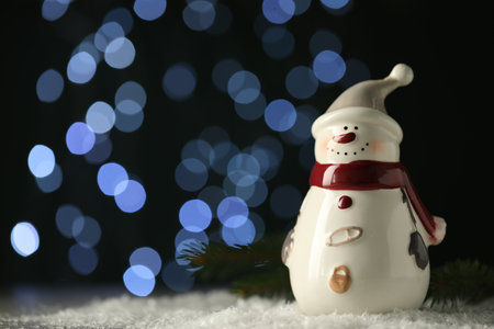 Cute decorative snowman on artificial snow against blurred lights. Space for textの写真素材