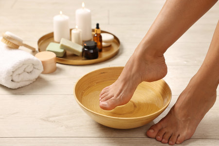 Woman soaking her feet in bowl with water on floor, closeup. Body careの写真素材