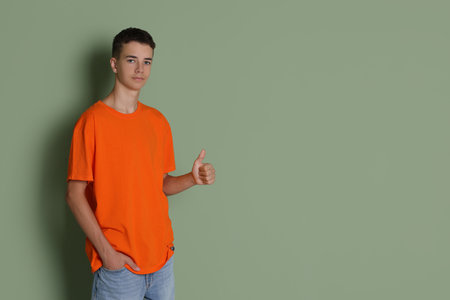 Teenage boy wearing orange t-shirt and showing thumbs up on green background, space for textの写真素材