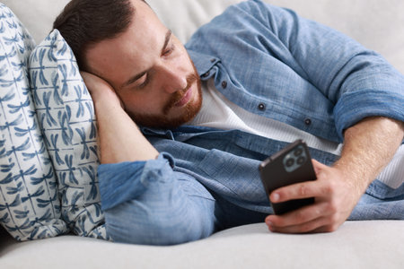 Person looking at smartphone while resting on sofaの写真素材