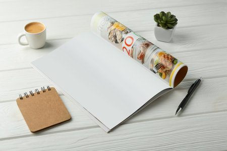 Open magazine with blank page, coffee, plant and stationery on white wooden table. Mockup for designの写真素材