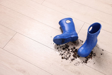 Rubber boots with mud on wooden floor. Space for text