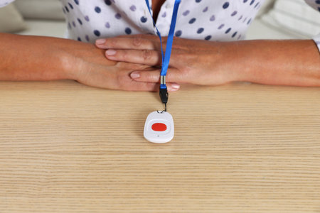 Senior woman with emergency call button at wooden table, closeup