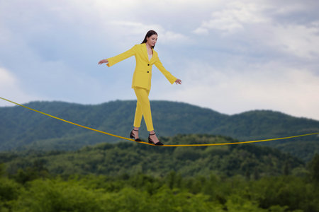 Businesswoman walking rope in mountains. Concept of risk and balance