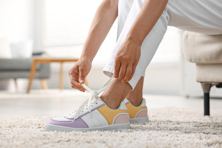 Woman tying shoelace of sneaker indoors, closeupの写真素材