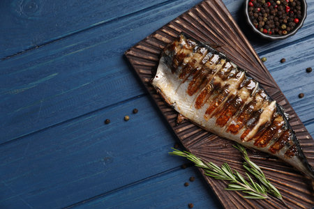 Board with delicious grilled mackerel, peppercorns and rosemary on blue wooden table, flat lay. Space for textの写真素材