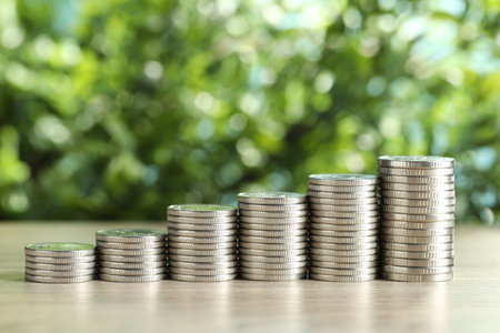 Stacked coins on light wooden table against blurred green background, closeup. Salary concept