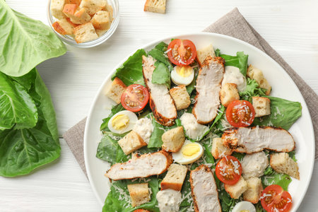 Tasty Caesar salad with chicken and tomatoes on white wooden table, flat layの写真素材