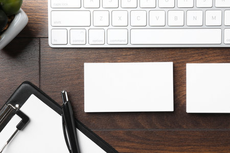 Blank business cards, clipboard with sheet, keyboard and pen on wooden table, flat lay. Mockup for designの写真素材