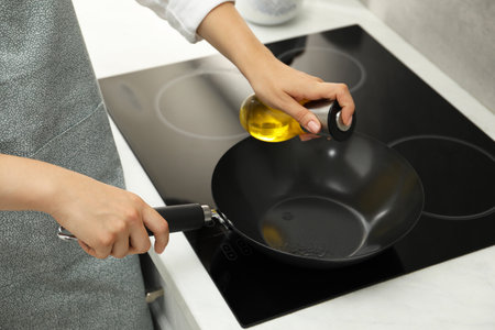 Woman with bottle of oil and frying pan in kitchen, closeupの写真素材