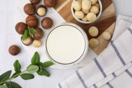 Glass of macadamia milk and nuts on white tiled table, flat layの写真素材