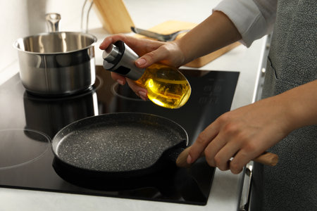 Woman with bottle of oil and frying pan in kitchen, closeupの写真素材