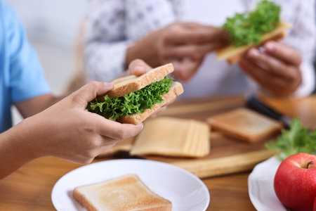 Boy and his mother preparing lunch box with healthy snacks at wooden table in kitchen, closeupの写真素材