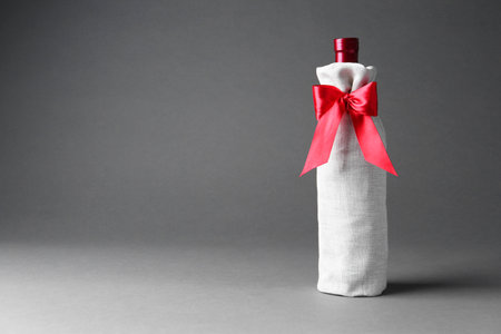Wine bottle in burlap package with red ribbon on gray background, space for textの写真素材