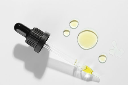 Cosmetic oil and pipette on light gray background, top view