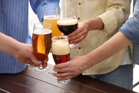 People with different types of beer clinking glasses at wooden table, closeupの写真素材