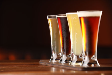 Glasses with different types of beer on wooden table against color background, closeup. Space for textの写真素材