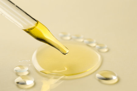 Cosmetic oil dripping from pipette on dark beige background, closeup. Space for textの写真素材
