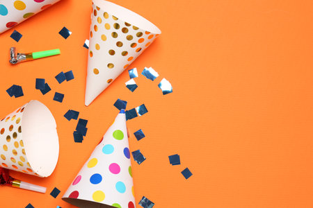 Shiny confetti, blowers and party hats on orange background, flat lay. Space for textの写真素材
