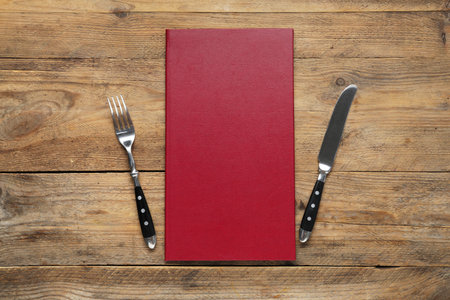 Hardcover menu and cutlery on wooden table, flat layの写真素材