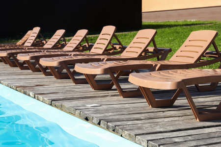 Empty sun loungers on wooden deck near outdoor swimming poolの写真素材