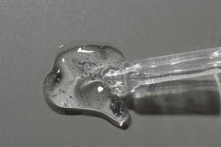 Dripping cosmetic serum from pipette on gray background, top view
