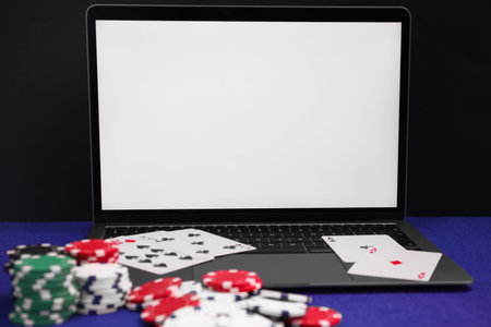 Laptop, poker chips and playing cards on blue table, closeup. Online game