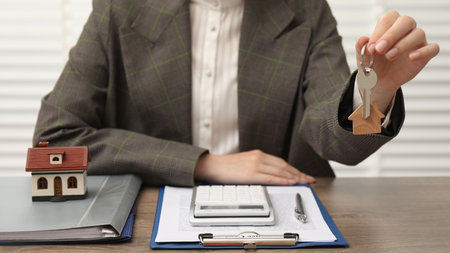 Real estate agent with house model, key and stationery at wooden table, closeupの写真素材
