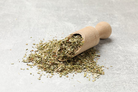 Wooden scoop with dried oregano on gray table, closeup