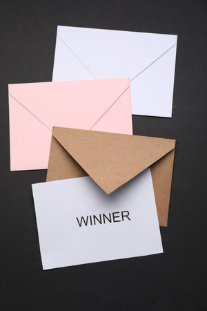 Card with word Winner and envelops on black background, flat lay