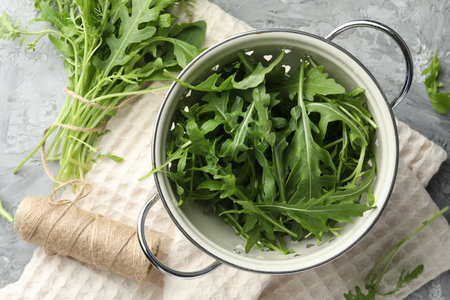 Fresh green arugula leaves in colander and spool of thread on gray table, flat layの写真素材
