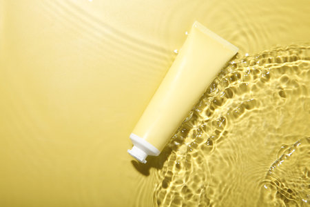 Tube with cream in water on yellow background, top view. Cosmetic productの写真素材