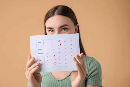 Woman holding calendar with marked menstrual cycle days on beige backgroundの写真素材