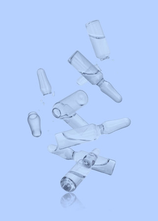 Many ampoules and glass pieces falling on light blue backgroundの写真素材