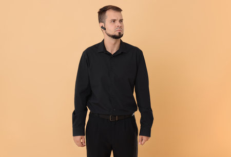 Young bodyguard with earpiece on beige backgroundの写真素材