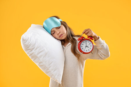Overslept girl with sleep mask, pillow and alarm clock on orange backgroundの写真素材