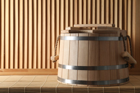 Sauna equipment. Bucket on bamboo bench near wooden wall, space for textの写真素材